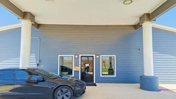 A building with a covered entrance, a car parked in front, and a blue exterior wall.