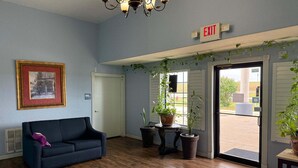 A room with a blue couch, a framed picture on the wall, a chandelier, potted plants, and an exit sign.