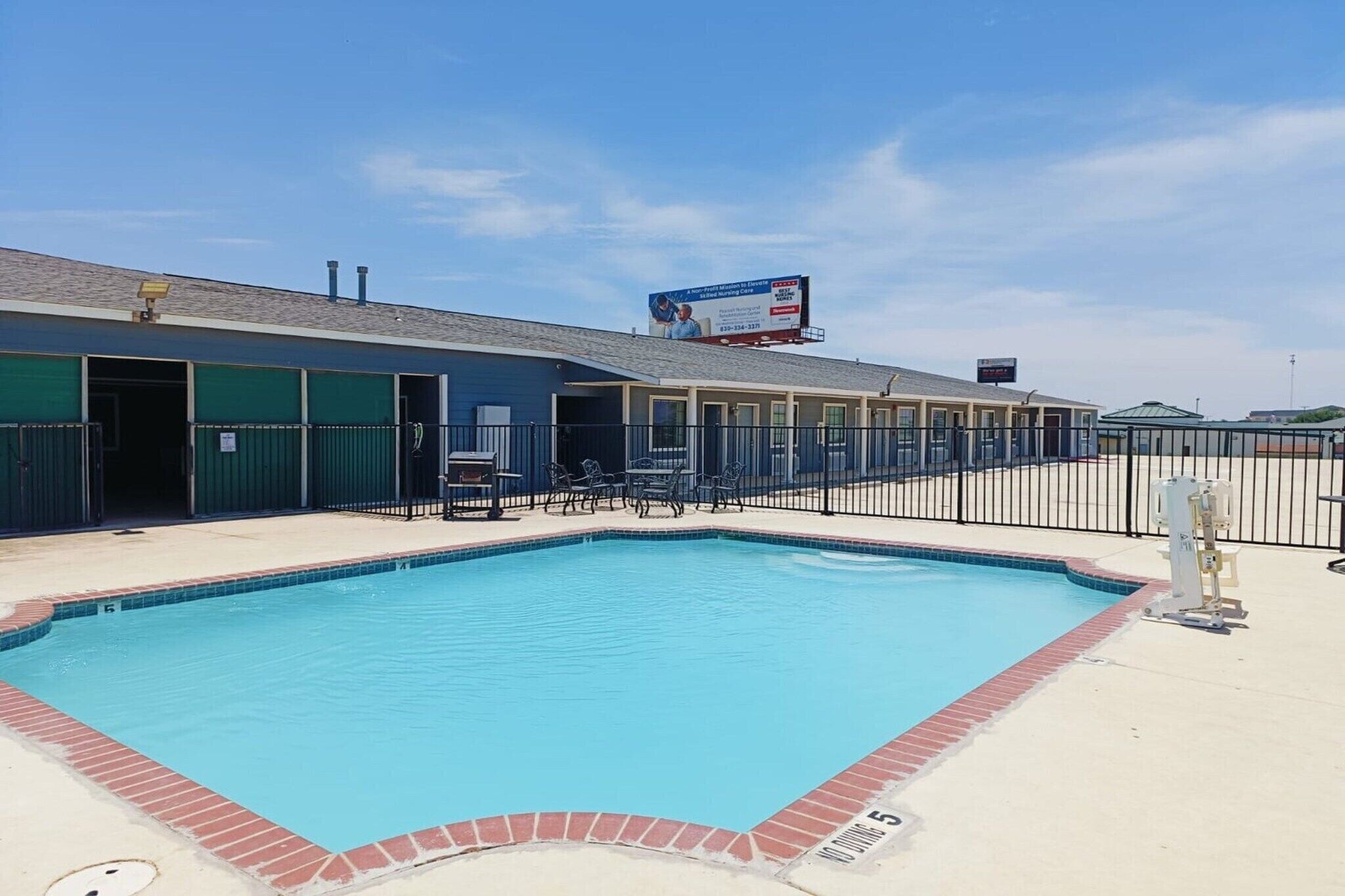 A swimming pool with a fenced area, a building with a billboard, and a clear sky.