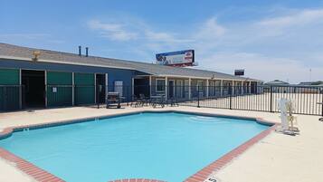 A swimming pool with a fenced area, a building with a billboard, and a clear sky.
