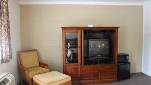 A room with a wooden cabinet containing a television, a small table, a chair, and a microwave.