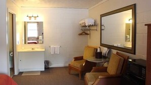 A small, compact room with a single bed, a bedside table, a chair, a mirror, and a microwave.