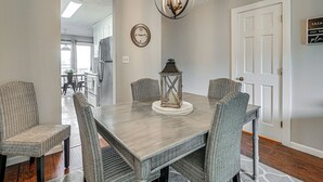 A dining room with a rectangular table, wicker chairs, a hanging light fixture, a clock, and a door with a sign. - Walk to Shore! Condo w/ Balconies in Myrtle Beach (Myrtle Beach)