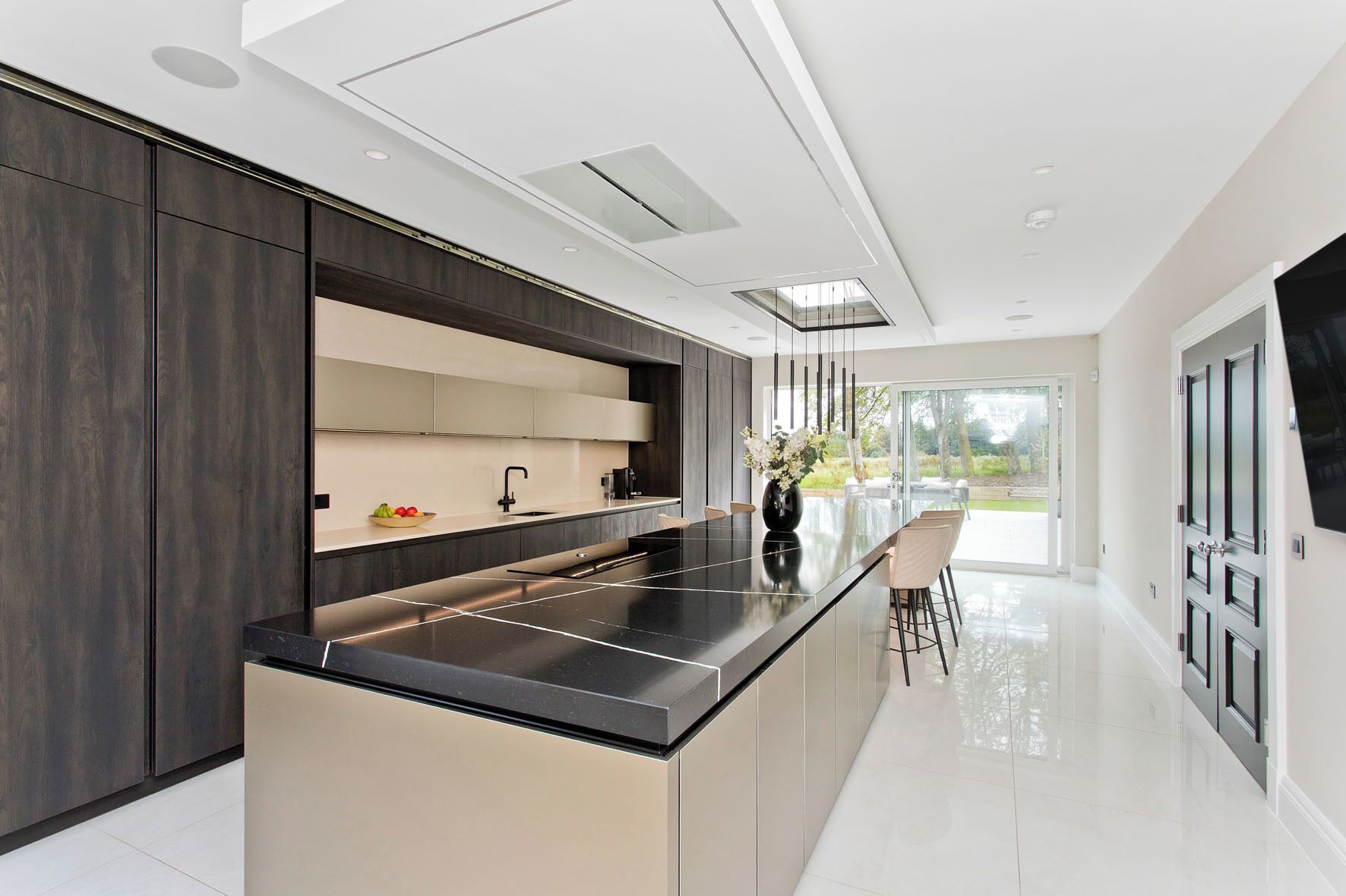 A modern kitchen with a central island, dark cabinetry, and a large window providing a view of the outdoors.