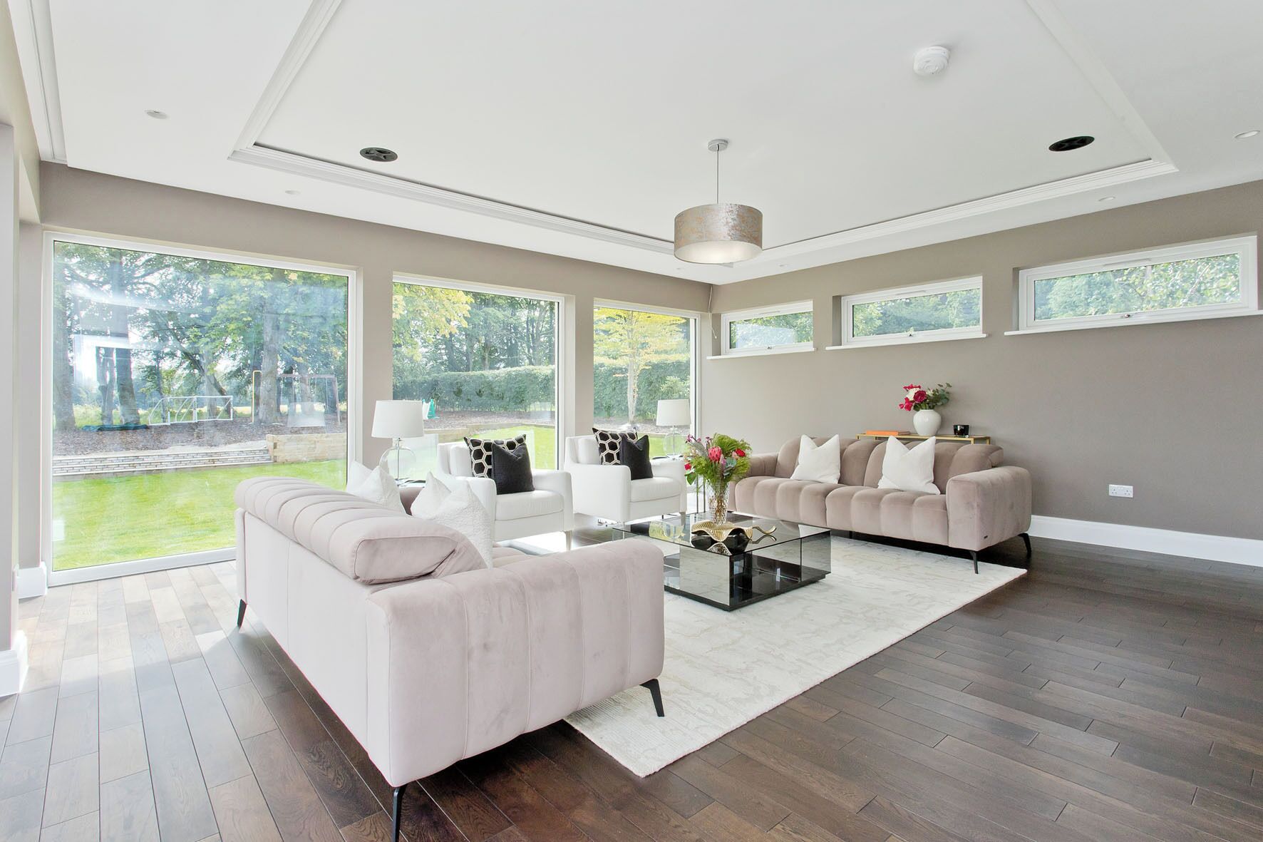 A spacious living room with a large window, a white sofa, a beige sofa, and a coffee table.