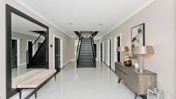 A hallway with a staircase, a bench, a console table with lamps, and a large mirror.