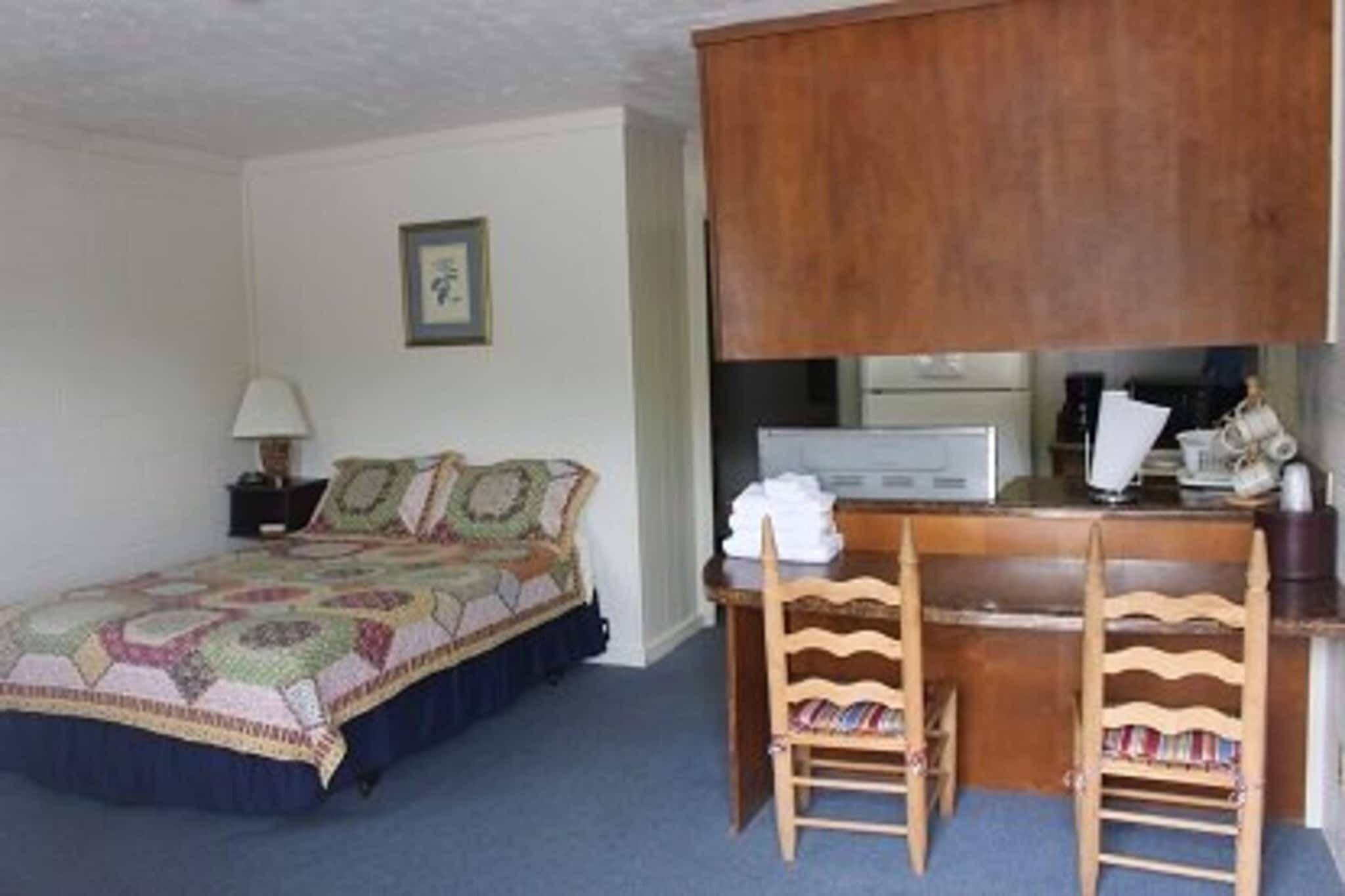 Une chambre à coucher avec un lit, un bureau avec une chaise, une lampe et un tableau encadré au mur.