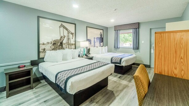 A hotel room with two beds, a desk, a chair, a wardrobe, and a window with curtains.