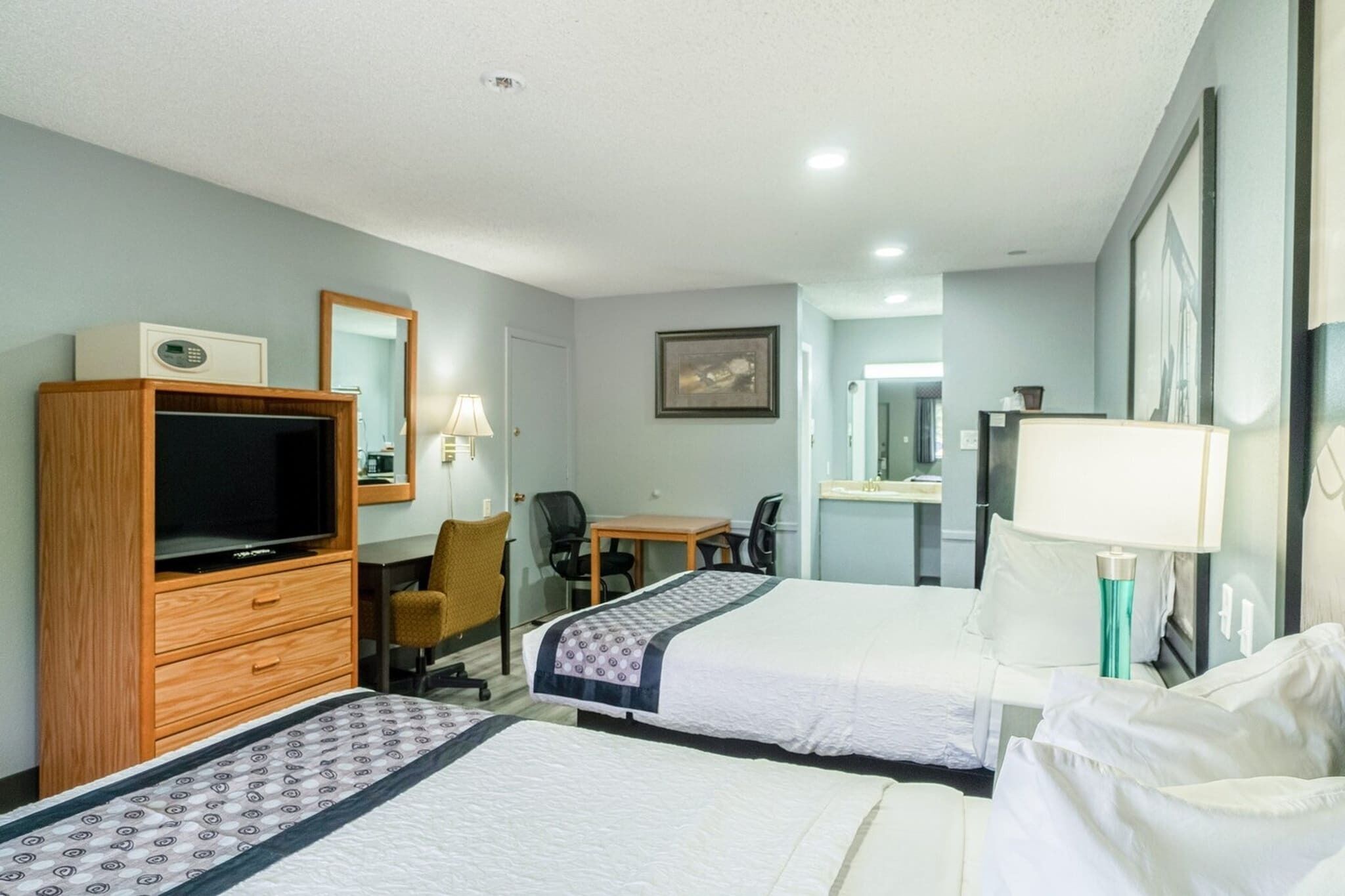 A hotel room with two beds, a TV, a desk, a chair, a lamp, and a mirror.