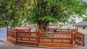 A wooden deck with a fence, a large tree, and a building in the background.