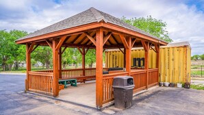 A wooden gazebo with benches and a trash can.