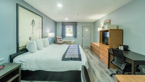 A hotel room with a bed, desk, TV, and a window with curtains.