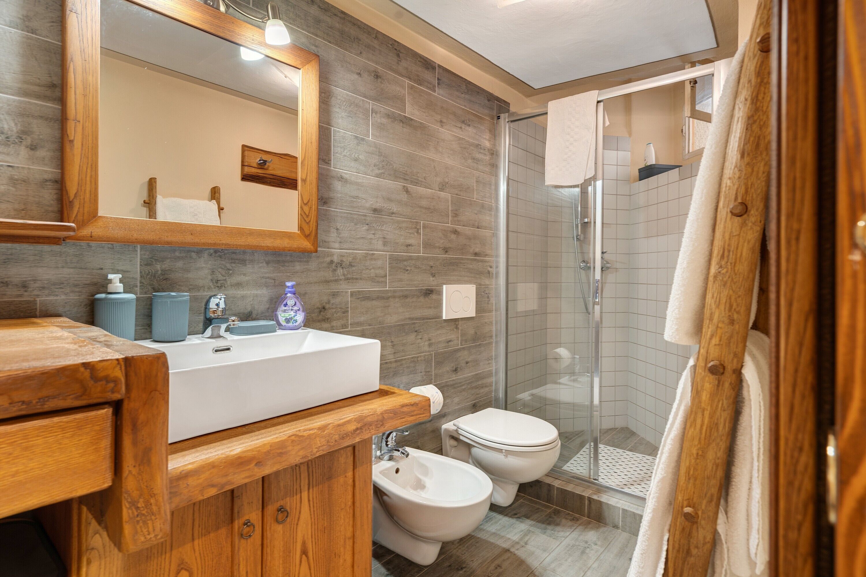 Een moderne badkamer met een houten wastafelmeubel, een douchecabine van glas en een wit toilet.