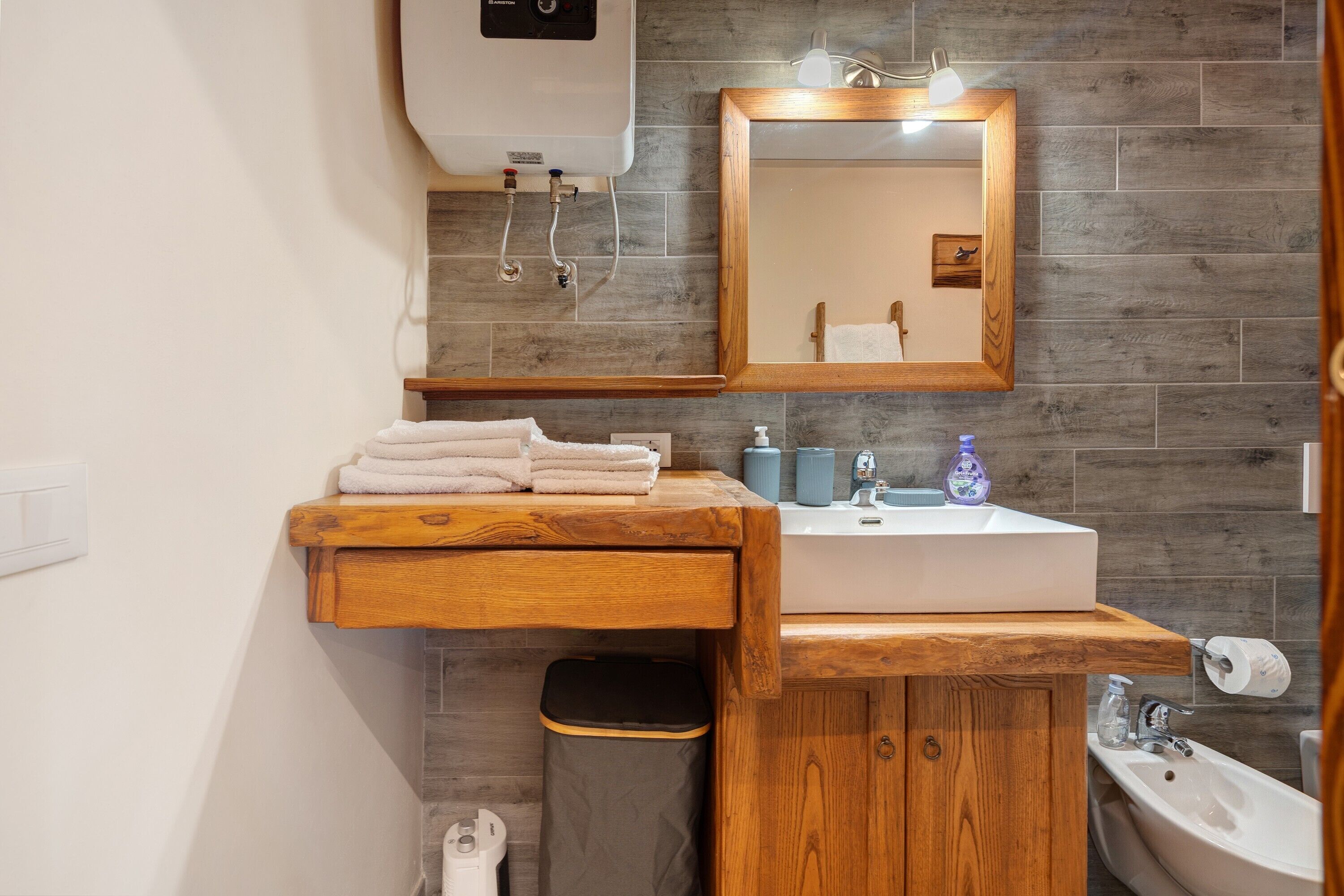 A bathroom with a wooden vanity, a sink, a mirror, and a toilet.