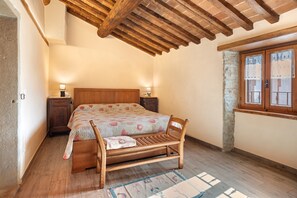 Ein Schlafzimmer mit einem hölzernen Bett, Nachttischen, einem Fenster mit Spitzenvorhängen und einer Steinwand.