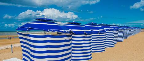A row of striped beach umbrellas on a sandy beach.