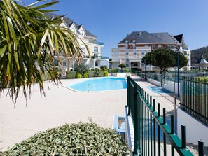 Ein Schwimmbad, umgeben von einem grünen Zaun, mit Gebäuden im Hintergrund.