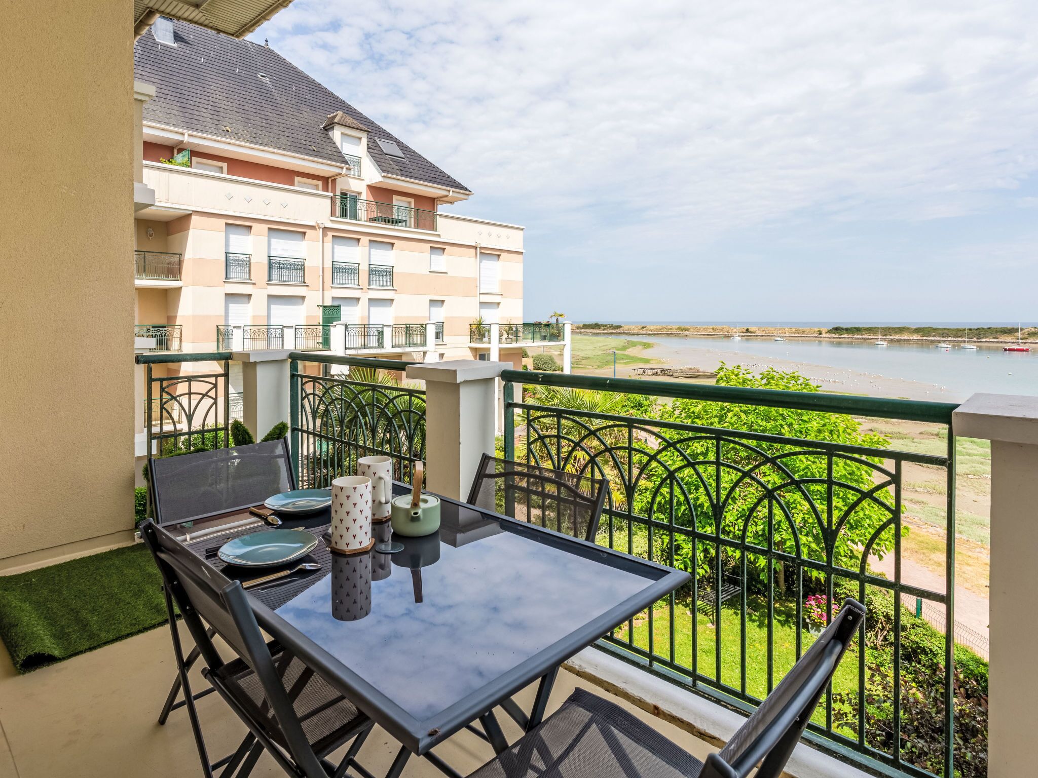 A balcony with a table and chairs, overlooking a body of water and a building.