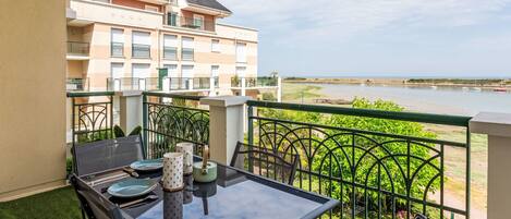 A balcony with a table and chairs, overlooking a body of water and a building.
