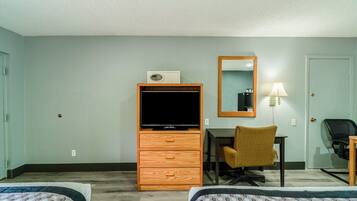 Habitación de hotel con dos camas, un aparador de madera con televisor, un escritorio con silla, un espejo y una lámpara.
