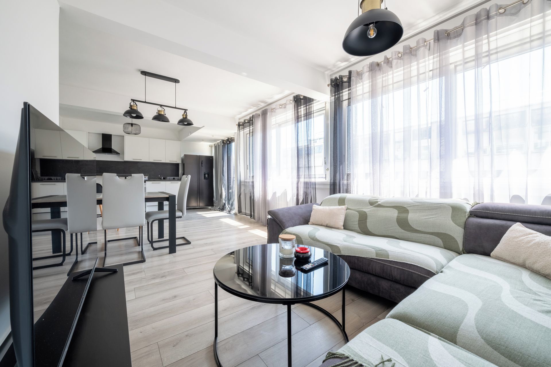 Een moderne woonkamer met een bank, een salontafel, en een eethoek met stoelen en een tafel.