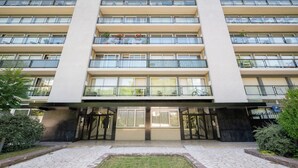 Un edificio a più piani con un ingresso centrale, balconi su ogni piano e un'area d'ingresso pavimentata.