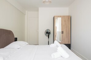 Ein Hotelzimmer mit einem Bett, einem Holzschrank, einem Standventilator und einer Tür.