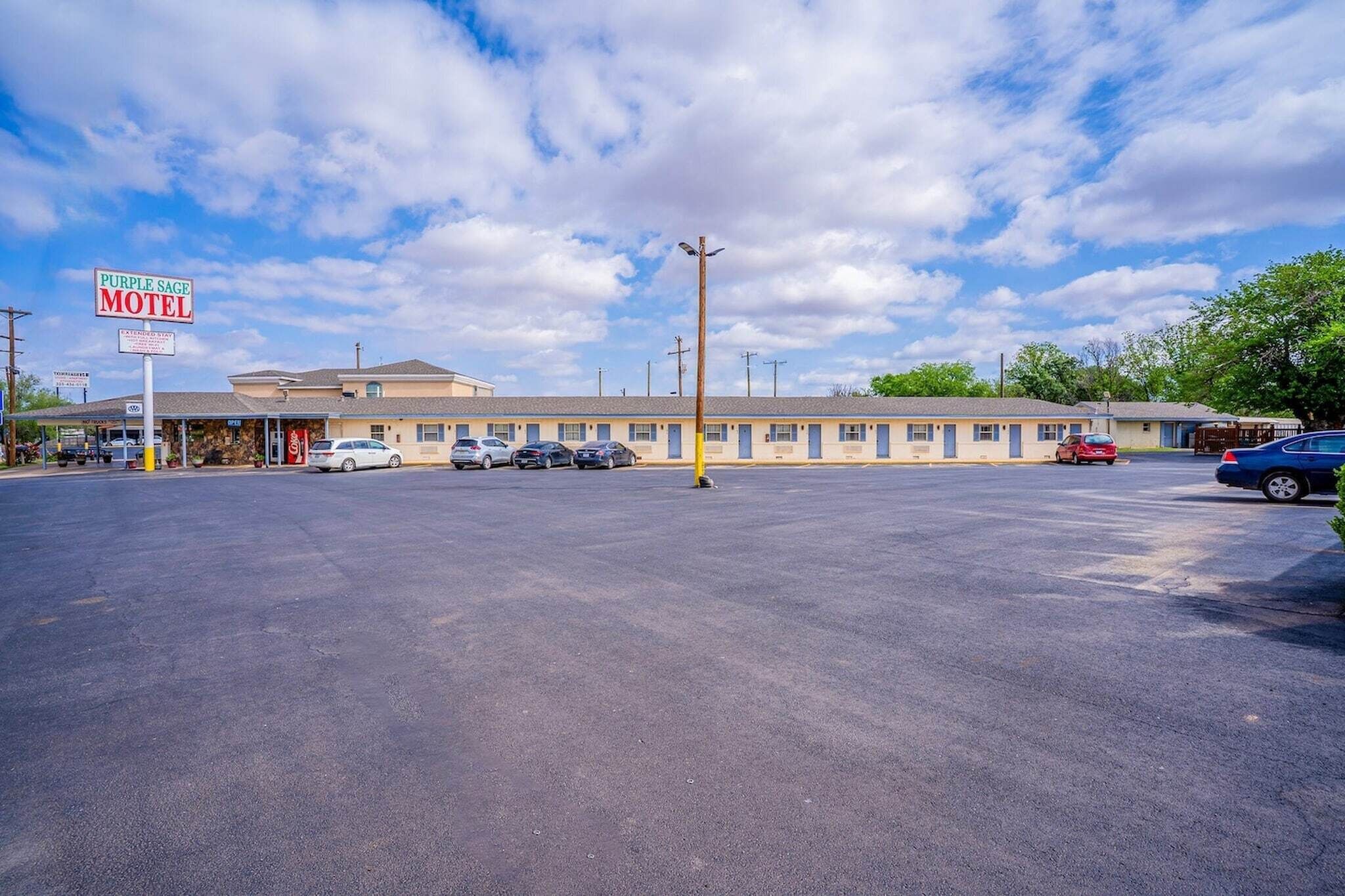 Un motel avec une rangée de chambres, un parking et un panneau indicateur.
