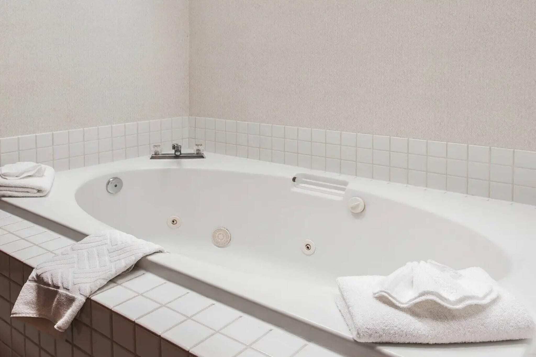 A white bathtub with a control panel, a towel on the side, and a tiled wall.