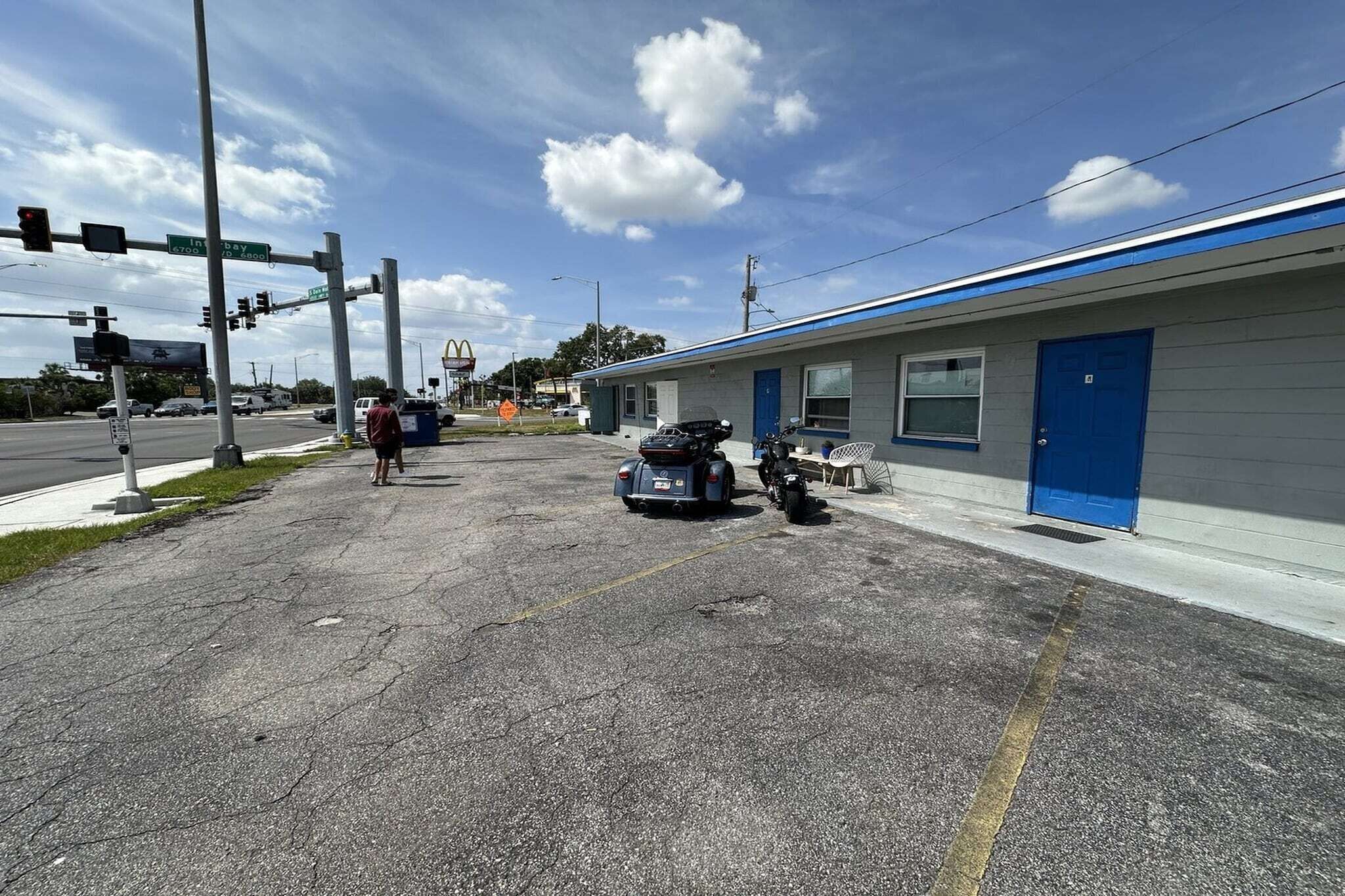 A motel with a blue exterior, a parking lot, and a street intersection with traffic lights.