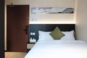 Habitación de hotel con cama, puerta de madera, mesita de noche y una obra de arte colgada en la pared.