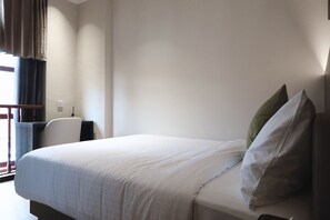 Una habitación de hotel con cama, escritorio, silla y ventana con cortinas.