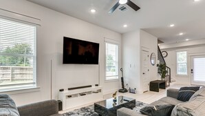 Una sala de estar moderna con un televisor de pantalla plana, sofás grises, una mesa de centro de vidrio y una escalera que conduce a otro nivel.