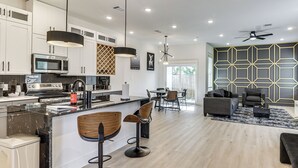 Una cocina moderna con una isla central, taburetes de bar y un comedor con sofá y sillas.