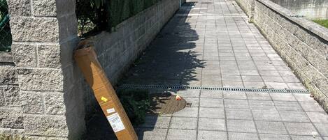 A sidewalk with a manhole cover, a stone wall, and a green fence.