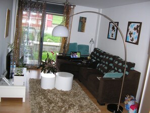 A living room with a sofa, a coffee table, a TV, a lamp, and a window with curtains.