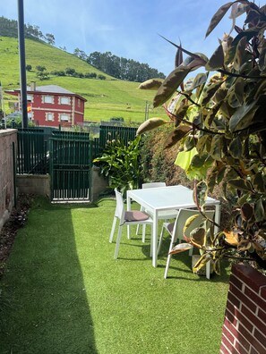 A patio with a white table and chairs, surrounded by green artificial grass. - Cozy 1-bedroom apartment with a garden (Miengo)