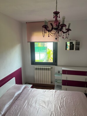 A bedroom with a bed, a radiator, a window with a view, a dresser, and a chandelier. - Cozy one-bedroom apartment with a garden (Miengo)