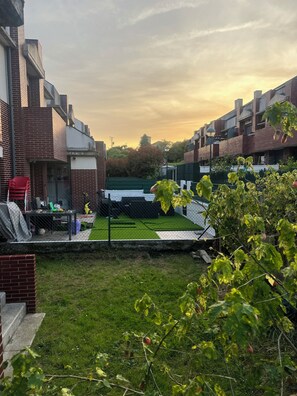 A residential area with brick buildings, a fenced yard, and a green artificial turf.