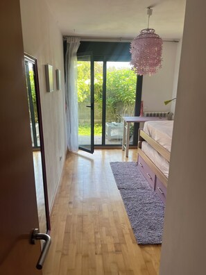 A bedroom with a bed, a desk, a chair, a window with a view of greenery, and a sliding glass door. - Cozy 1-bedroom apartment with a garden (Miengo)