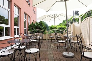 Une terrasse extérieure avec des tables et des chaises, un sol en briques et un bâtiment doté de grandes fenêtres.