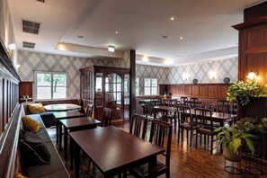 Un vaste espace dédié à la salle à manger, avec des tables et des chaises en bois, un banc intégré agrémenté de coussins et de grandes fenêtres laissant entrer la lumière naturelle.