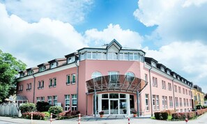 Un hôtel à plusieurs étages, doté d’une façade rose, de grandes fenêtres et d’une entrée abritée.