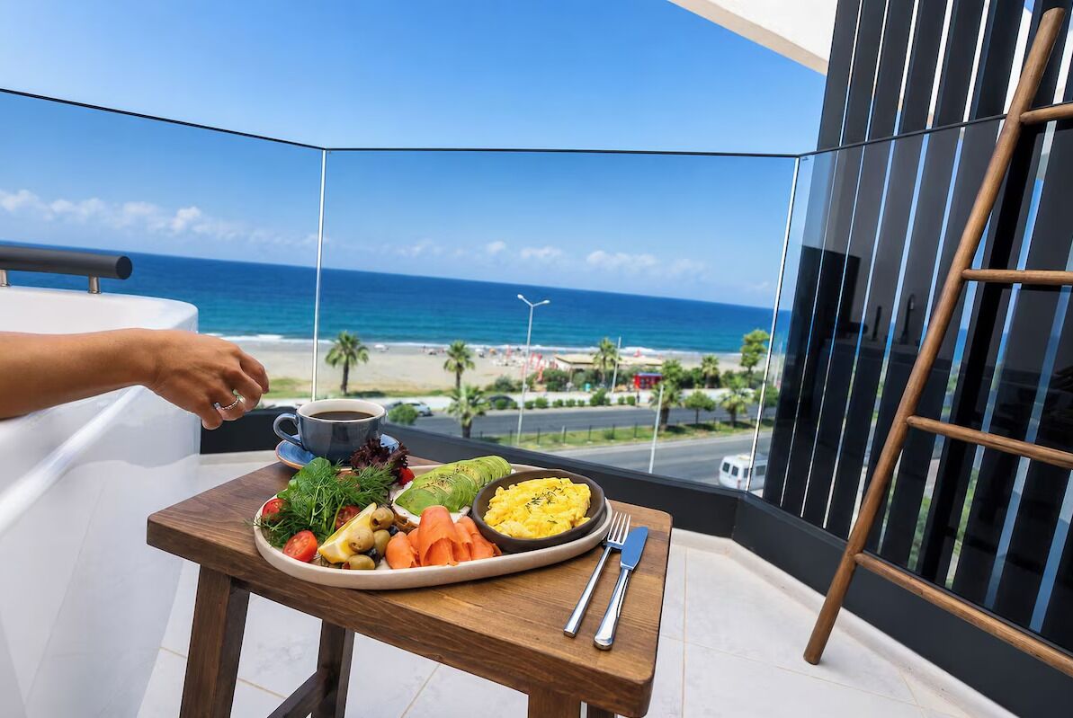 A balcony with a dining table, a plate of food, a cup, and a view of the beach and ocean.