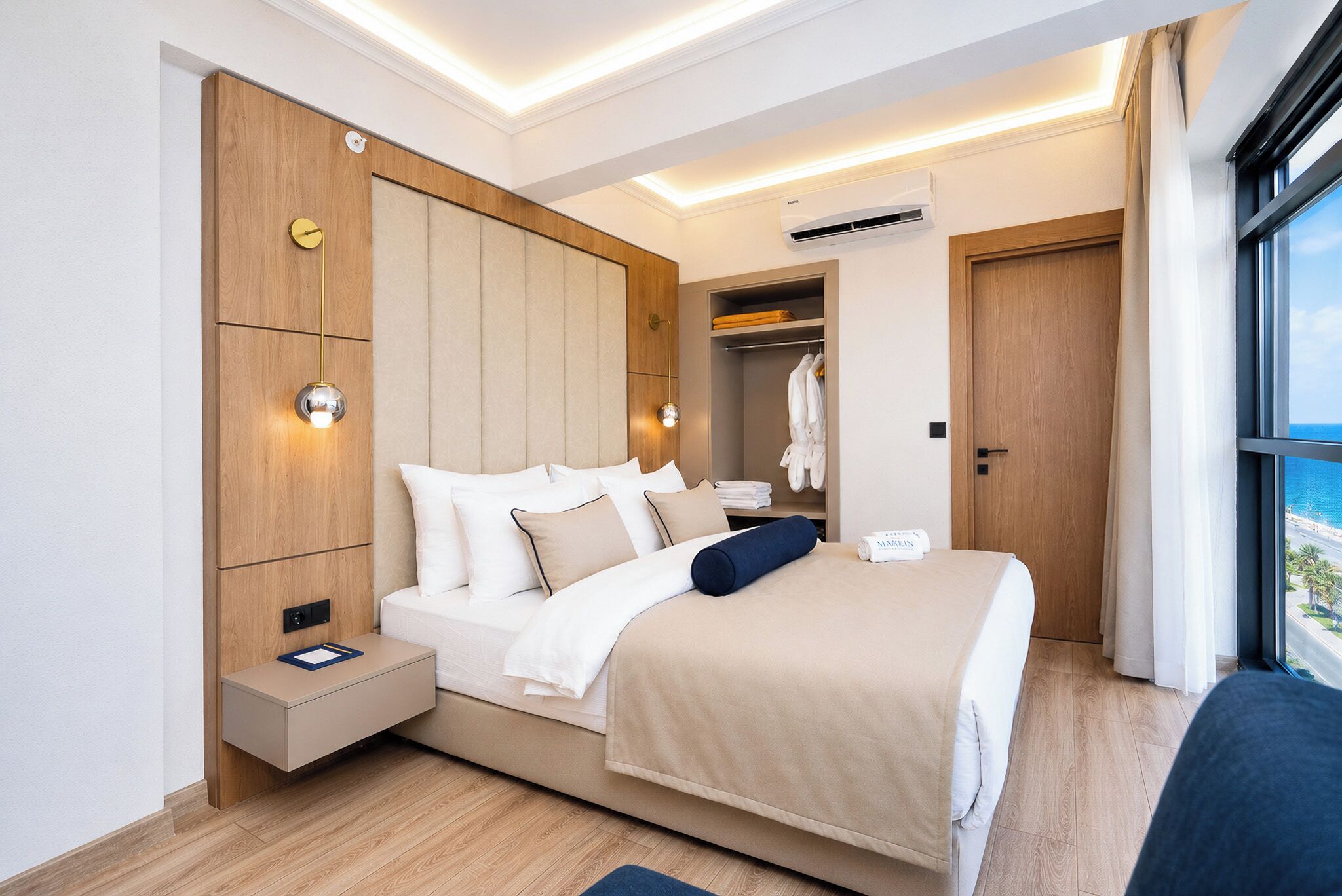 A modern hotel room with a bed, bedside table, wardrobe, and an air conditioning unit.