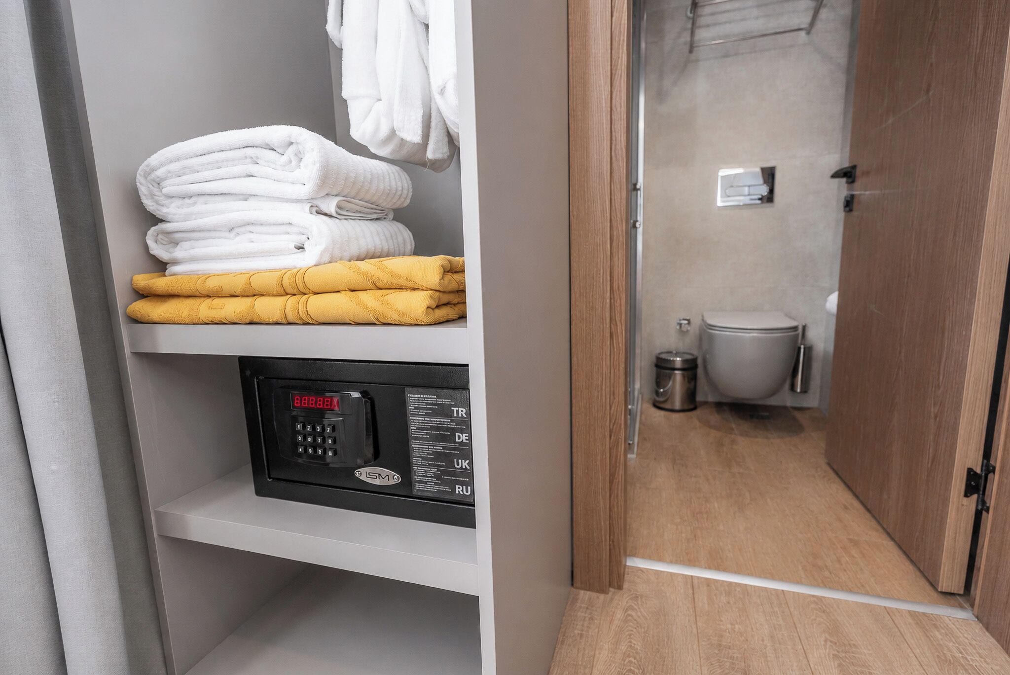 A bathroom with a toilet, a trash bin, and a towel rack with white and yellow towels.