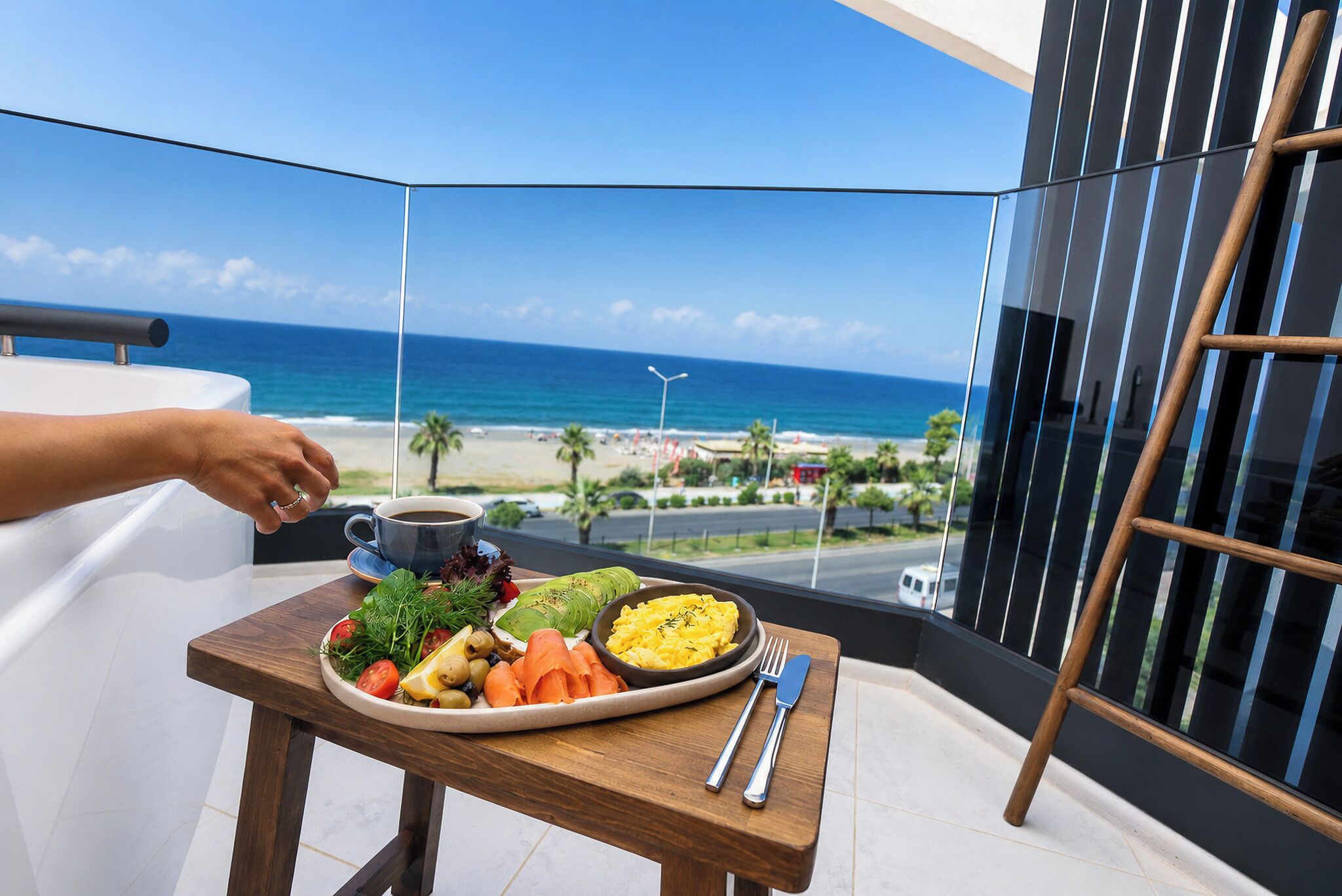 Ein Balkon mit Esstisch, einer Speisenplatte, einer Tasse und Blick auf Strand und Meer.