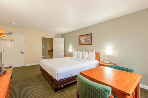 Quarto de hotel com cama, escrivaninha, cadeira, cômoda, espelho e um quadro na parede.