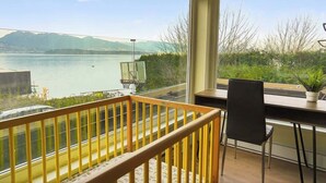 Habitació amb vista a un llac, un balcó amb barana de fusta, un escriptori amb una cadira i una planta en test.