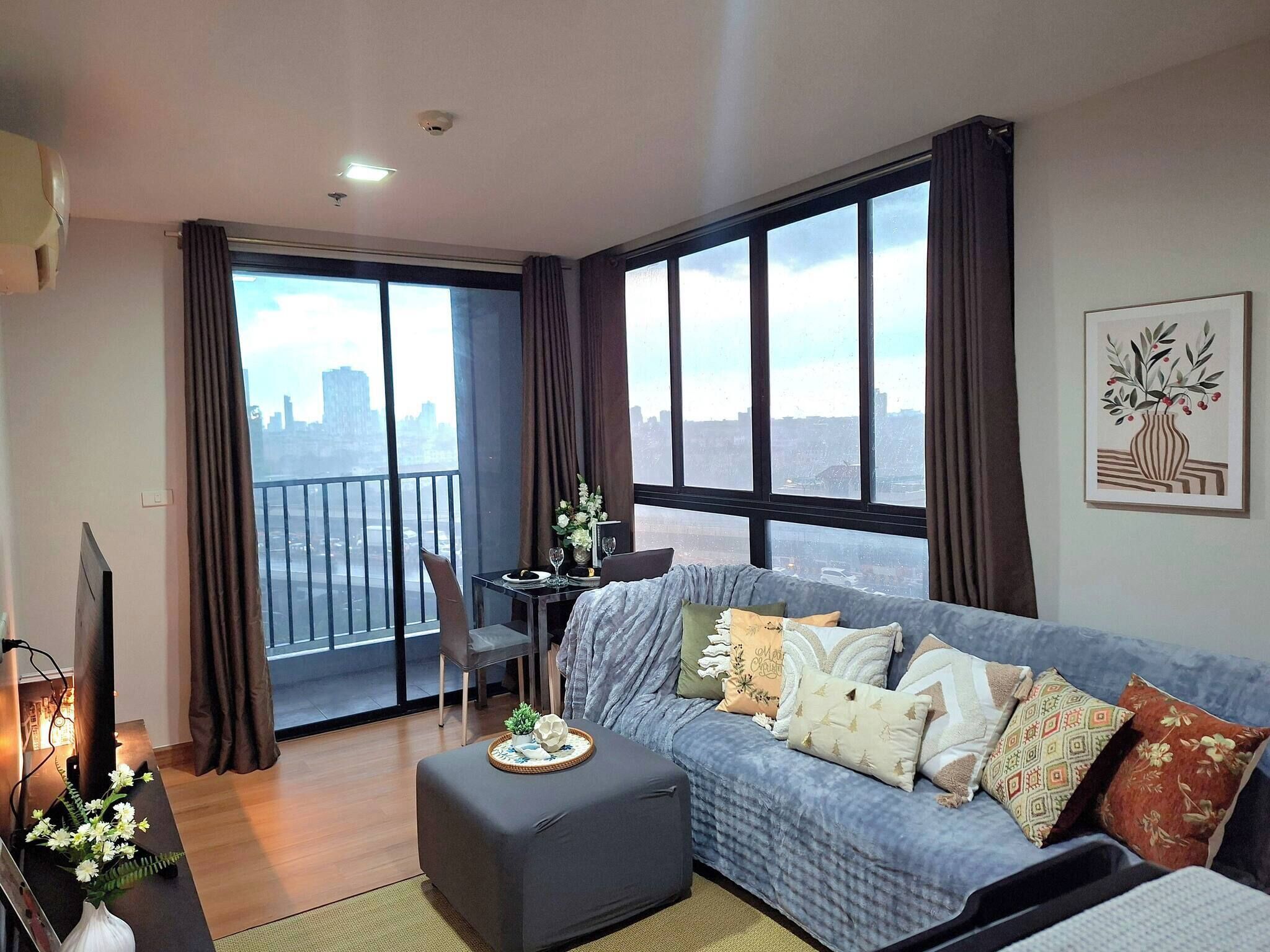 A living room with a sofa, a small table, a TV, and a balcony with a city view.